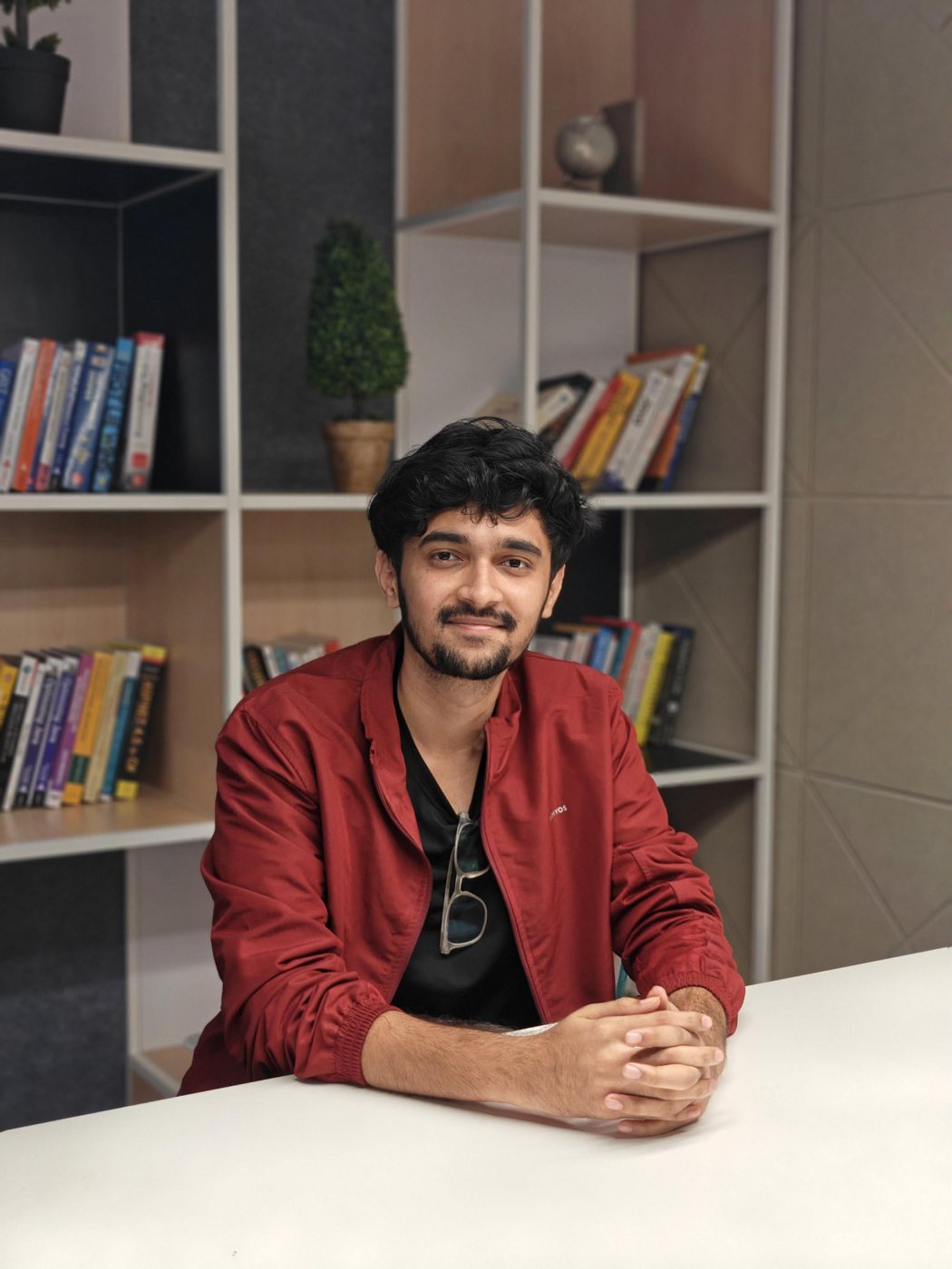 Gopal Bagaswar, in front of a bookshelf arranged mostly by color